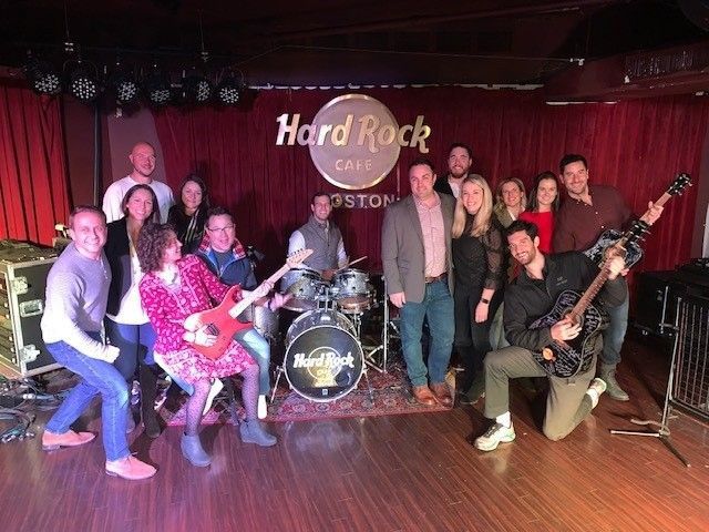 Apty team members posing for a photo on the stage with instruments at the Hard Rock Cafe